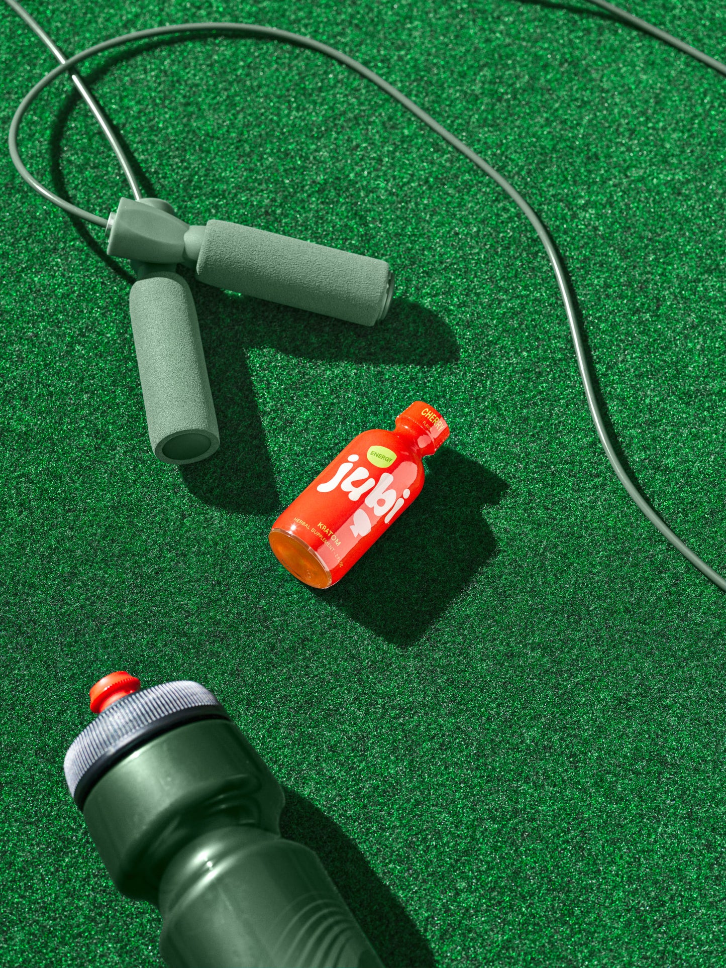 Jubi Cherry kratom shot with jump rope and bottle on turf.