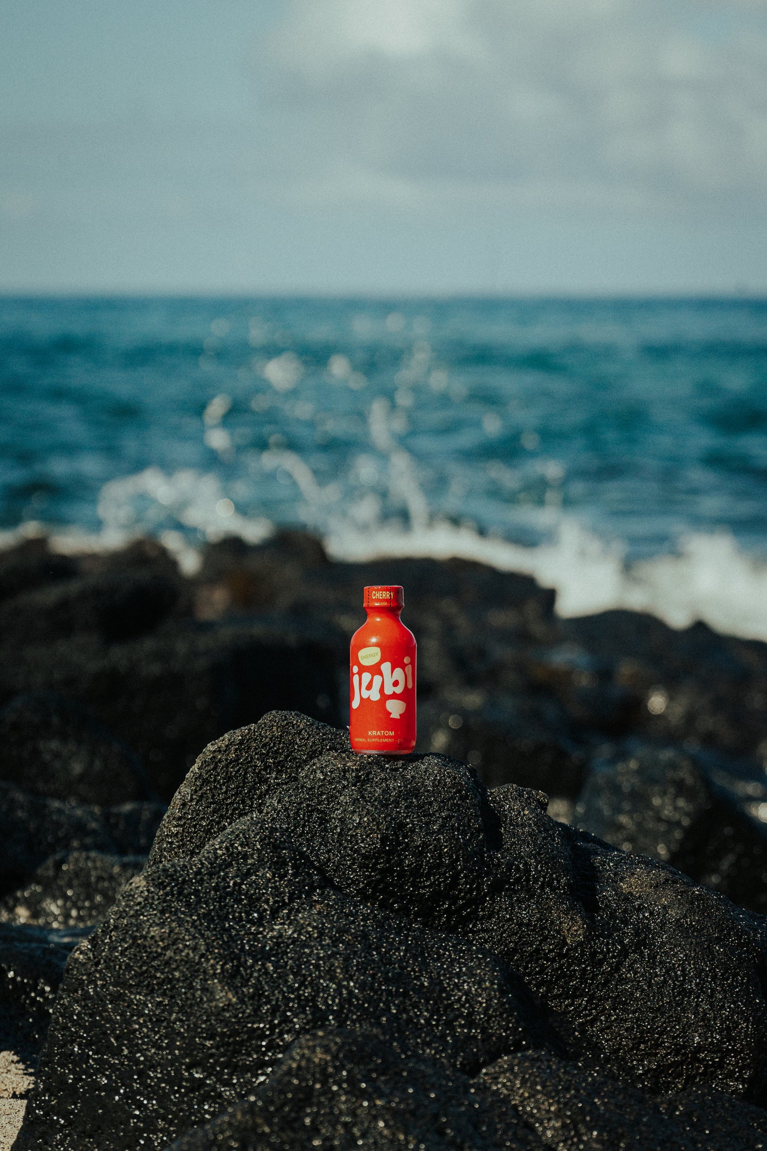 Jubi Cherry Energy Shot on oceanfront rocks.