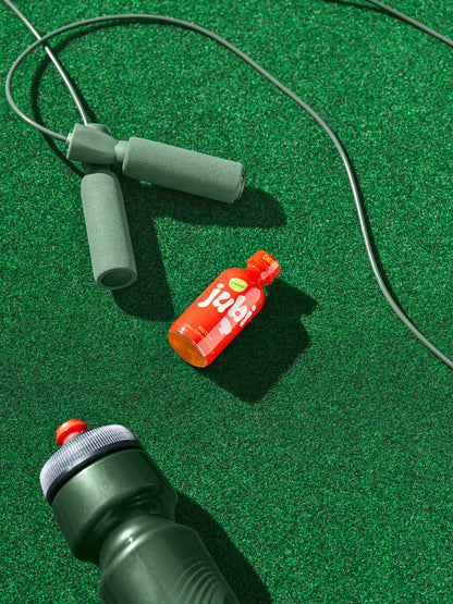 Jubi Cherry kratom shot with jump rope and bottle on turf.